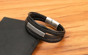 Detail of multi-layer braided leather bracelet for men with silver metal buckle on wood