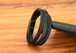 Close-up of multilayer braided black leather bracelet with textured metal charm and magnetic clasp