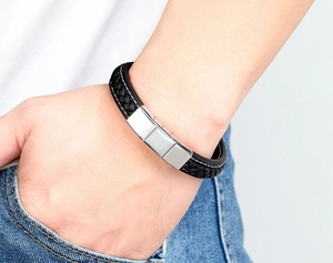 Detail of black braided leather bracelet with silver magnetic clasp and white stitching