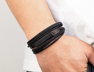 Macro detail of men's multilayer braided leather bracelet with black textured metal charm