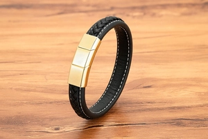 Detail of black woven leather bracelet with white stitching and gold metal magnetic clasp