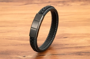 Macro detail of braided black leather bracelet with white stitching and matte magnetic buckle