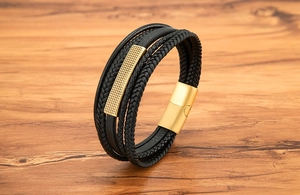 Detail of multi-layer black braided leather bracelet with gold textured metal clasp on wood