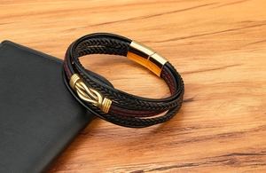 Dettaglio di bracciale in pelle intrecciata a più strati con cuciture rosse e chiusura oro