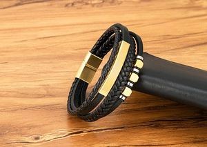 Detail eines mehrlagigen schwarzen Lederarmbands mit goldener Metallplatte und Magnetverschluss