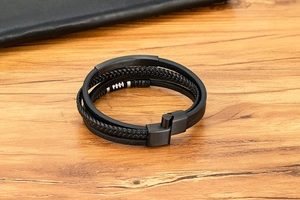 Detail eines mehrlagigen schwarzen Lederarmbands mit Edelstahlverschluss auf Holzgrund