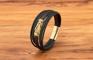 Dettaglio di un bracciale in pelle nera multistrato con cuciture rosse e fibbia a U d'oro