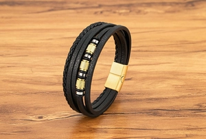 Detalle de pulsera de cuero negro multicapa con cuentas doradas y cierre magnético