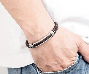 Detail van een gevlochten bruine leren armband met een zilveren roestvrijstalen accent