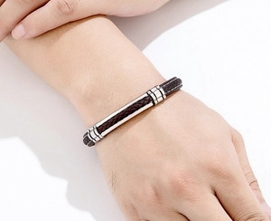 Detail van een bruine gevlochten leren armband voor heren met gepolijste stalen plaat