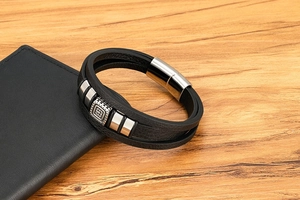 Dettaglio di un bracciale multistrato in pelle nera con elemento quadrato in metallo e chiusura magnetica