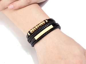 Detail eines mehrlagigen schwarzen Lederarmbands mit goldenem Metallrohr und Magnetverschluss