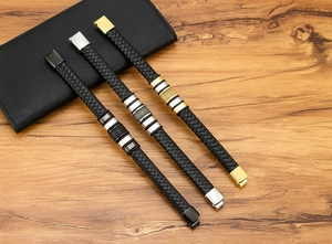 Detail view of woven leather bracelets with black, silver and gold metal clasps on wood