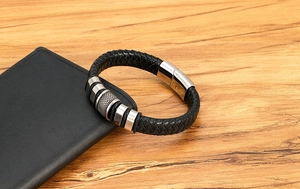 Detail of black braided leather bracelet with silver metal rings on a wooden desk