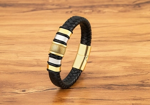 Detail of woven black leather bracelet with textured gold cylinder and magnetic clasp