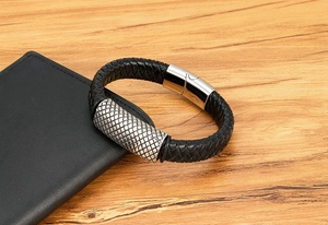 Detail of woven black leather bracelet with textured silver metal cylinder and clasp