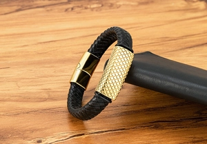 Detail of black braided leather bracelet with gold magnetic clasp and textured metal
