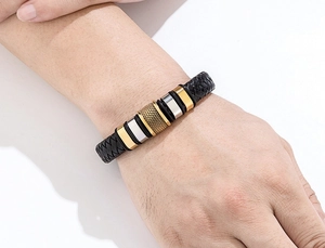 Close-up of black braided leather men's bracelet with gold honeycomb metal beads