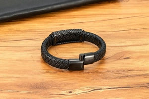 Close-up of black braided leather bracelet featuring a textured magnetic steel clasp on wood