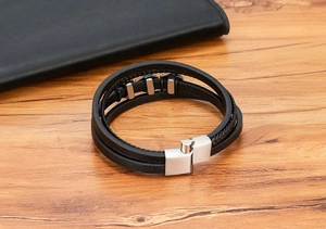 Detail eines mehrlagigen schwarzen Lederarmbands mit gebürstetem Metallverschluss auf Holz