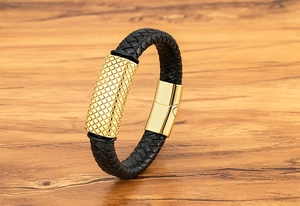 Close-up of black braided leather bracelet featuring a textured gold metal cylinder charm
