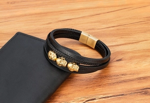 Nahaufnahme eines mehrlagigen Lederarmbands mit goldenen Totenköpfen auf Holzoberfläche