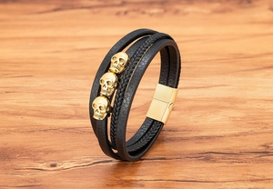 Detailansicht eines schwarzen Lederarmbands mit goldenen Totenköpfen und Magnetverschluss