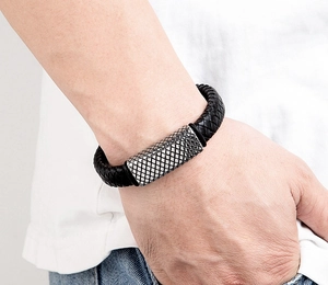 Close-up of men's black braided leather bracelet with textured silver metal clasp detail