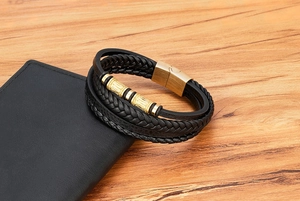Detalle de pulsera multicapa para hombre en cuero negro con detalles en metal dorado