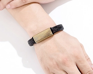 Macro detail of the golden cylindrical metal bead with diamond pattern on braided leather strap