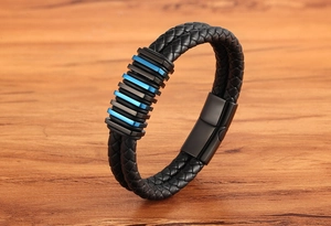 Dettaglio del bracciale in pelle intrecciata con anelli metallici blu su legno