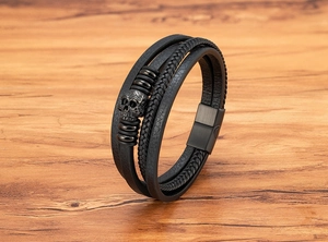 Detail of multilayer leather bracelet with skull charm on natural wood background