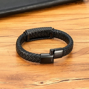Men's black braided leather bracelet with engraved black metal clasp on wood background
