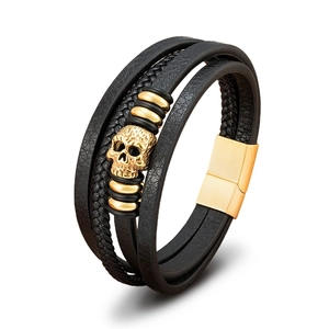 Detailed close-up of a multilayer black leather bracelet featuring a gold skull charm