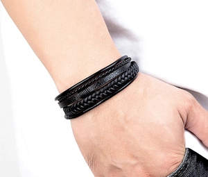 Close-up of a men's multi-layered black braided leather bracelet worn on a wrist