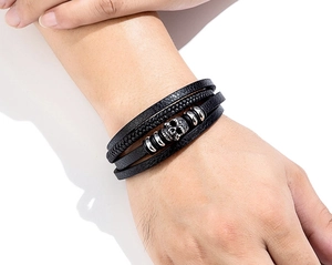 Detail of multi-layer black leather bracelet with silver skull charm on a model's wrist