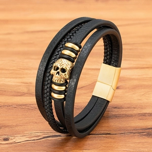Multi-layer black leather bracelet with golden skull charm on a light wooden background