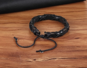 Dettaglio del bracciale in pelle intrecciata nera con cordino regolabile su legno