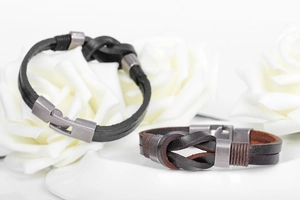 Macro shot of men's leather bracelets with metal clasp and knot design on white flowers