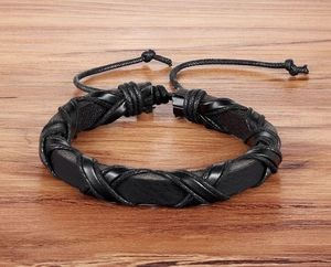 Dettaglio del bracciale in pelle nera intrecciata con cordino regolabile su legno