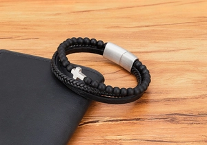 Dettaglio del bracciale multistrato in pelle con chiusura magnetica e croce su legno