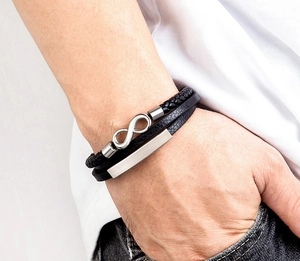 Detailansicht eines mehrlagigen schwarzen Lederarmbands mit Unendlichkeitssymbol am Handgelenk
