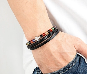 Dettaglio di un bracciale multistrato da uomo con perline colorate, croce d'argento e pelle nera