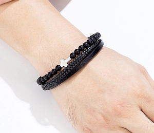 Dettaglio del bracciale multistrato in pelle nera e perline con croce sul polso