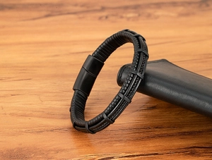 Close-up of black braided leather men's bracelet with matte magnetic clasp on wood