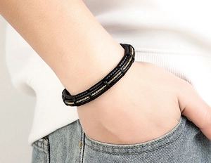 Close-up of men's black leather woven bracelet with gold chain detail worn on wrist