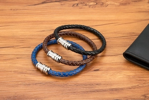 Macro shot of three braided leather bracelets with polished metal magnetic clasps on wood