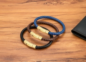 Detailopname van gevlochten lederen armbanden in blauw, bruin en zwart met gouden sluiting