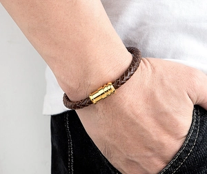 Close-up of a braided dark brown leather bracelet with a gold magnetic cylinder clasp
