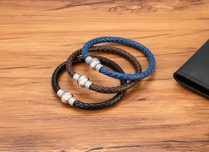Dettaglio di bracciali intrecciati in pelle nera, marrone e blu con chiusura magnetica in acciaio